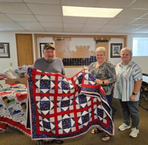 Pictured left to right: Gordy Edington receiving the quilt donation from Tammy Schultz-Lemmer and Terri Verhasselt.